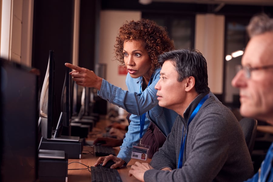 An instructor pointing something out on a computer to an adult student